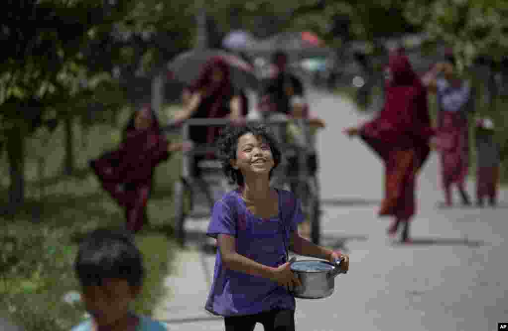A girl runs with a container to join a line of people, ahead of Buddhist monks, who push a cart loaded with cooked food containers. The food is part of what the monks received as daily alms from devotees in Hlaing Thaya, northwest of Yangon, Myanmar. 