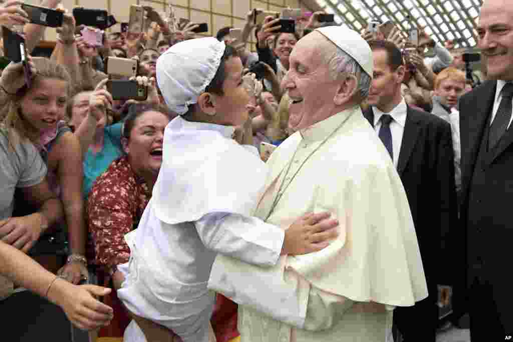 Paus Fransiskus mengangkat seorang anak laki-laki yang berpakaian seperti dirinya pada acara mingguan bertemu masyarakat umum di Vatikan.