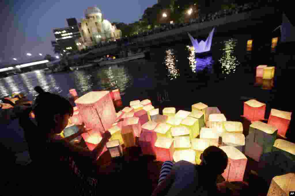 Anak-anak berdoa setelah melepaskan lampion kertas di Sungai Motoyasu, tempat ribuan korban bom atom tewas, dengan latar belakang Kubah Bom Atom di Hiroshima, Jepang bagian barat (6/8). (AP/Eugene Hoshiko)