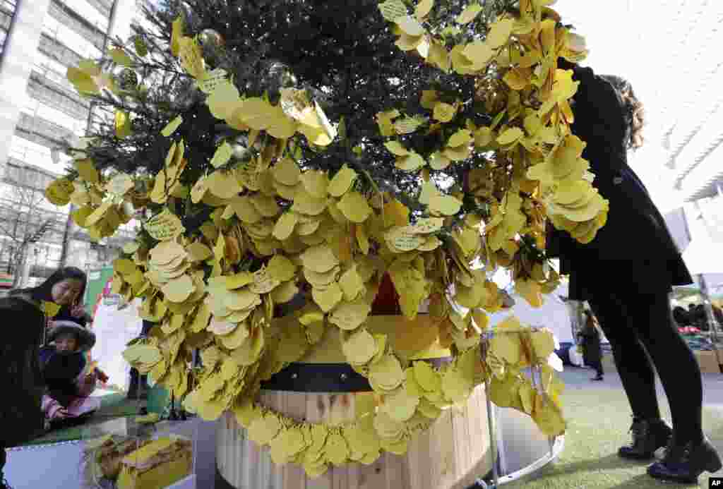 A woman hangs a paper bearing her New Year wishes to a tree in Seoul, South Korea, Dec. 31, 2014.