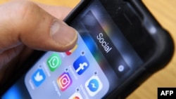 Seorang pria memegang ponsel pintar dengan ikon untuk aplikasi jejaring sosial Facebook, Instagram dan Twitter terlihat di layar di Moskow pada 23 Maret 2018. (Foto: AFP)