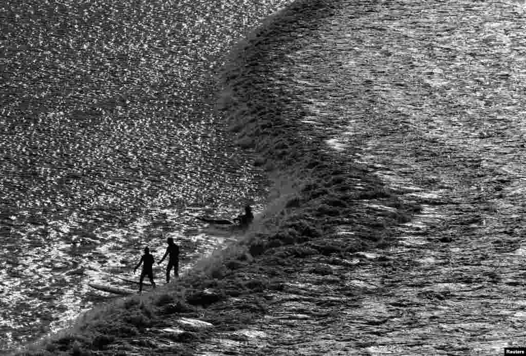 Surfers and canoeists ride a Severn Bore surge wave, a natural phenomenen where a set of waves push through the Severn River estuary and upstream, being largest around the times of the equinoxes and just after full and new moons, in Newnham, Britain.