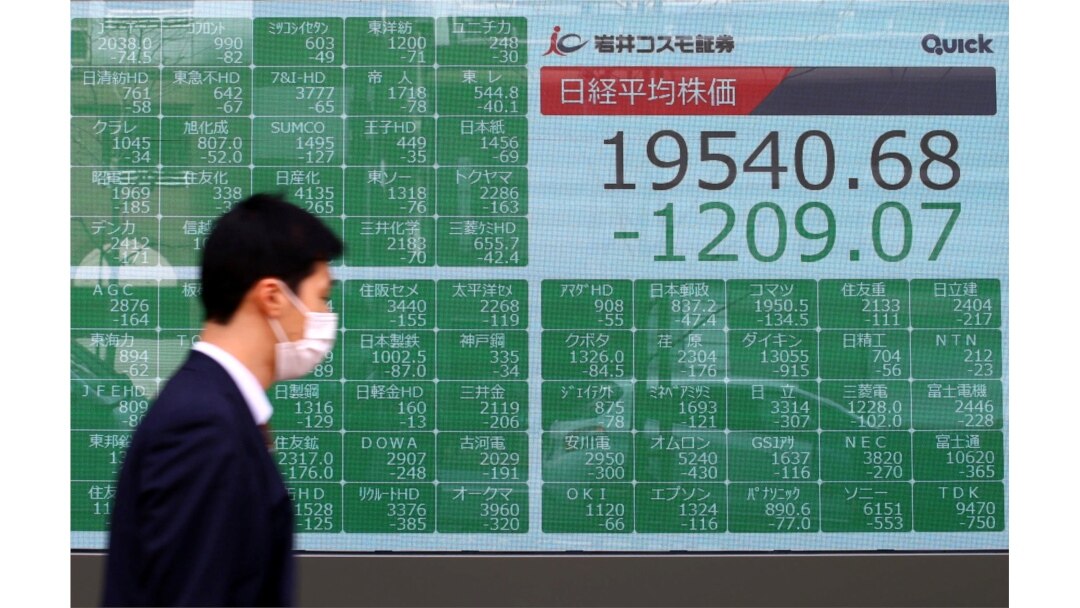 A passerby wearing a protective face mask following an outbreak of the coronavirus disease (COVID-19), walks past an electronic display showing Asian markets indices outside a brokerage in Tokyo, Japan, March 9, 2020.