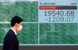 A passerby wearing a protective face mask following an outbreak of the coronavirus disease (COVID-19), walks past an electronic display showing Asian markets indices outside a brokerage in Tokyo, Japan, March 9, 2020.