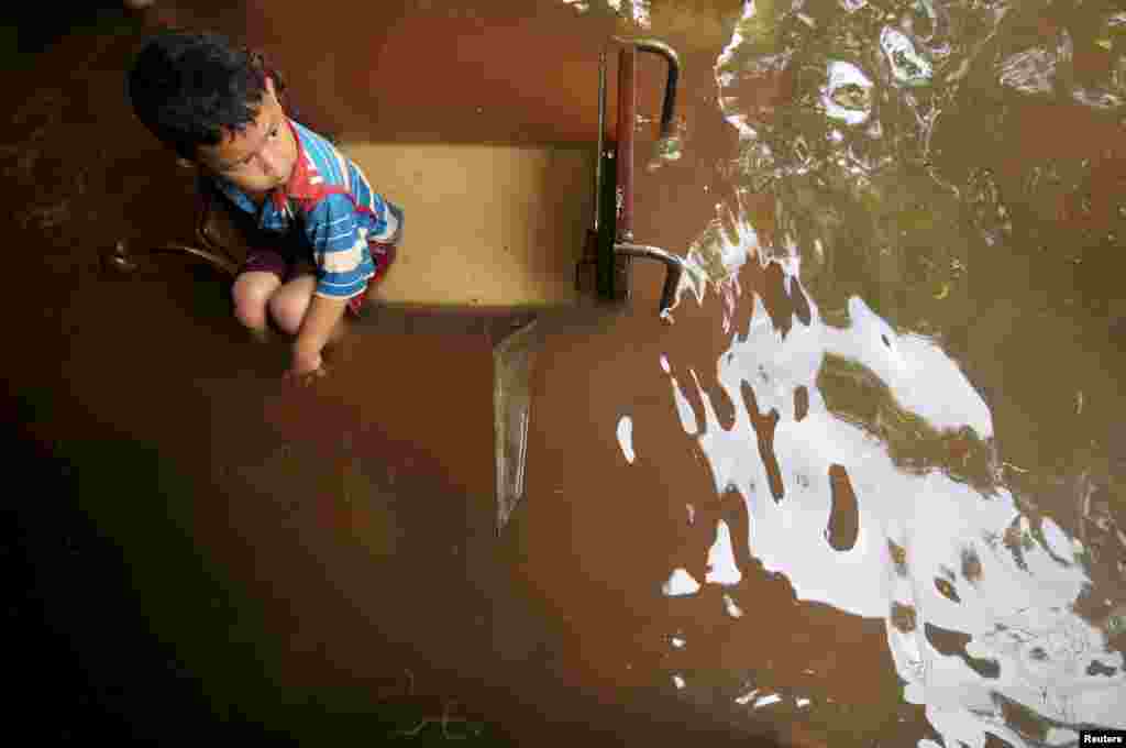 Seorang anak kecil duduk di kursi sementara banjir menghampiri rumahnya di desa Sidakaton, Tegal, Jawa Tengah (foto: Antara).