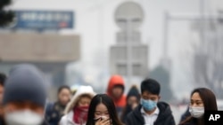 A woman uses a scarf and others wear masks to cover their face from pollutants as they walk along a street on a polluted day in Beijing, Tuesday, Dec. 8, 2015.