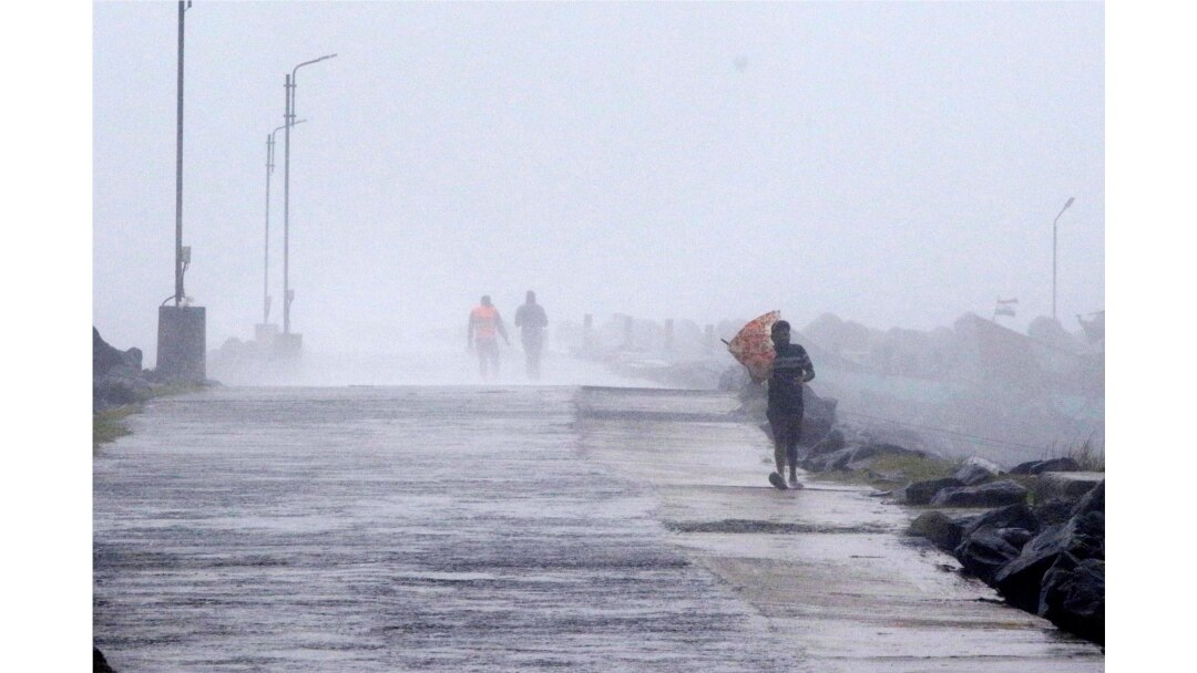 Seorang pria memegang payungnya, mencoba melawan angin kencang di Pelabuhan Kasimedu di pantai Teluk Bengal, Chennai, India, Rabu, 25 November 2020.