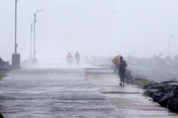 Seorang pria memegang payungnya, mencoba melawan angin kencang di Pelabuhan Kasimedu di pantai Teluk Bengal, Chennai, India, Rabu, 25 November 2020.