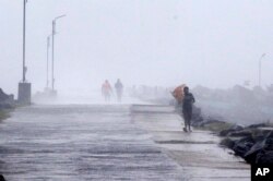 Seorang pria memegang payungnya, mencoba melawan angin kencang di Pelabuhan Kasimedu di pantai Teluk Bengal, Chennai, India, Rabu, 25 November 2020.