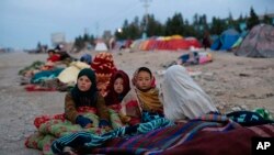 FILE - Afghan children are covered with a blanket as their families camp outside the Directorate of Disaster, in Herat, Nov. 29, 2021.