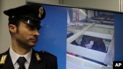 FILE - A police officer stands by a monitor projecting images of migrants crammed into a truck during a press conference at the police headquarters in Milan, Italy, Jan. 30, 2017.