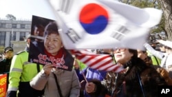 A supporter of impeached South Korean President Park Geun-hye waves flags of the U.S. and South Korea while another holds a portrait of the president during a rally in Seoul, South Korea, Feb. 27, 2017.