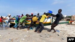 Quelques personnes tirent une pirogue en bois sur les rives du port de pêche traditionnel de Soumbedioune, à Dakar, le 2 juillet 2015. 