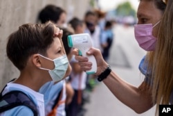 ARCHIVO - Una maestra con mascarilla para protegerse contra la propagación del coronavirus revisa la temperatura de su alumno en la escuela Maestro Padilla al comienzo del nuevo año escolar, en Madrid, el 7 de septiembre de 2021 (AP)