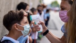 FILE - A teacher wearing a face mask to protect against the spread of coronavirus checks the temperature of her student at Maestro Padilla school as the new school year begins, in Madrid, Sept. 7, 2021. (AP)