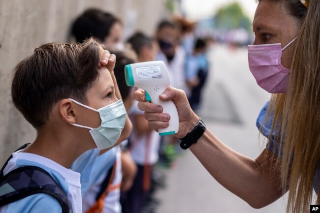 FILE - A teacher wearing a face mask to protect against the spread of coronavirus checks the temperature of her student at Maestro Padilla school as the new school year begins, in Madrid, Sept. 7, 2021. (AP)