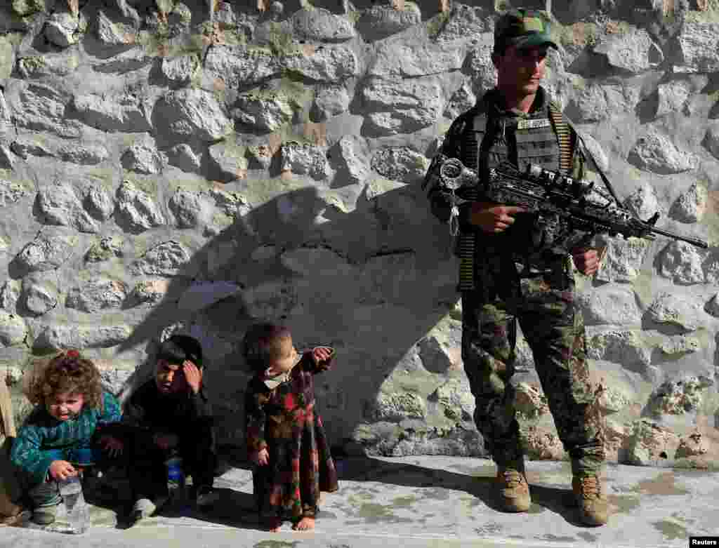 A member of the Afghan security forces watches along with family members of IS militants who surrendered to the government in Achin district of Nangarhar province, Afghanistan.