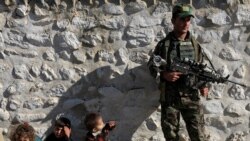 Seorang anggota pasukan keamanan Afghanistan mengawasi para militan ISIS yang menyerah kepada pemerintah, sementara anak-anak dari keluarga militan berada di dekatnya, di distrik Achin, provinsi Nangarhar, Afghanistan (17/11).