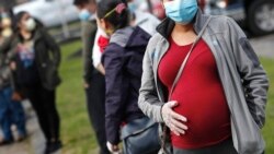 FILE: A pregnant woman wearing a face mask and gloves holds her belly as she waits in line for groceries at St. Mary's Church in Waltham, Massachussetts, May 7, 2020. The CDC urged all pregnant women on Aug. 11, 2021 to get the COVID-19 vaccine