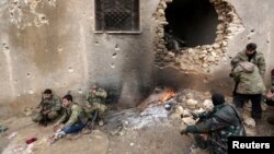 Rebel fighters rest near a hole in the wall by a fire on the outskirts of the northern Syrian town of al-Bab, Jan. 15, 2017. 