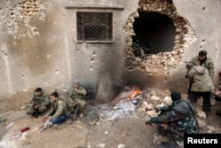 FILE - Rebel fighters rest near a hole in the wall by a fire on the outskirts of the northern Syrian town of al-Bab, Jan. 15, 2017.