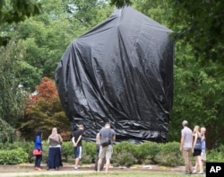 FILE - Residents and visitors look over the covered statue of Confederate General Robert E. Lee in Emancipation park in Charlottesville, Va., Aug. 23, 2017.