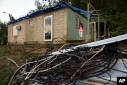In this Dec. 22, 2017 photo, Melanie Oliveras González stands on the porch of her house, behind a handful of electric cables knocked down by the winds of Hurricane Maria, in Morovis, Puerto Rico.