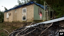 In this Dec. 22, 2017 photo, Melanie Oliveras González stands on the porch of her house, behind electric cables knocked down by the winds of Hurricane Maria, in Morovis, Puerto Rico.