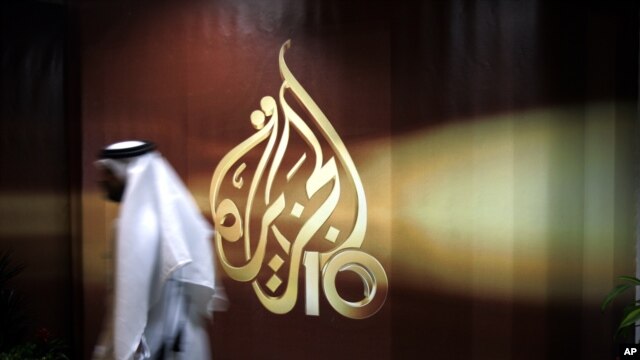 FILE - An employee of the Qatar-based Al-Jazeera network passes by an Al-Jazeera logo at the network's offices in Doha, Qatar.