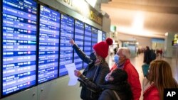 FILE - Passengers look at a flight information screen inside a terminal of the Barcelona Airport, Dec. 1, 2021.