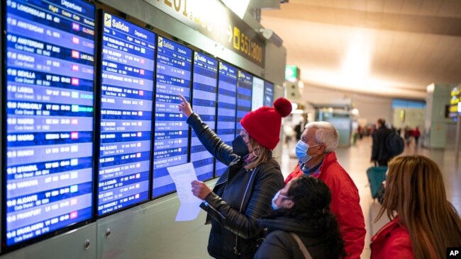 FILE - Passengers look at a flight information screen inside a terminal of the Barcelona Airport, Dec. 1, 2021.