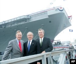FILE - President George W. Bush, center, with former President George H.W. Bush, left, and Florida Governor Jeb Bush, right, pose in front of the aircraft carrier George H.W. Bush after participating in the christening ceremony in Newport News, Va.
