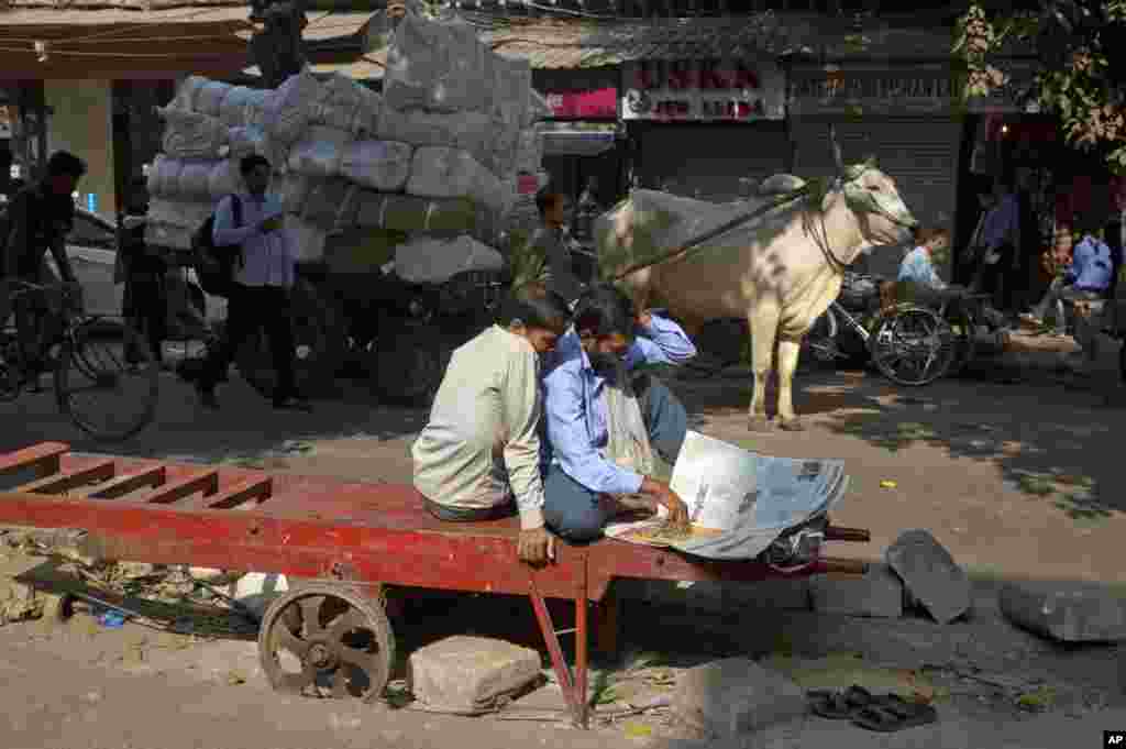 Daily wage laborers read a newspaper siting on their handcart at a market in New Delhi.