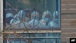 FILE - Members of a World Health Organization team are seen through a window wearing protective gear during a field visit to the Hubei Animal Disease Control and Prevention Center for another day of field visit in Wuhan in central China's Hubei province, on Feb. 2, 2021. 