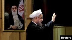 FILE - Iranian President Hassan Rouhani waves as he stands next to a portrait of Iran's Supreme Leader Ayatollah Ali Khamenei, Dec. 21, 2015.