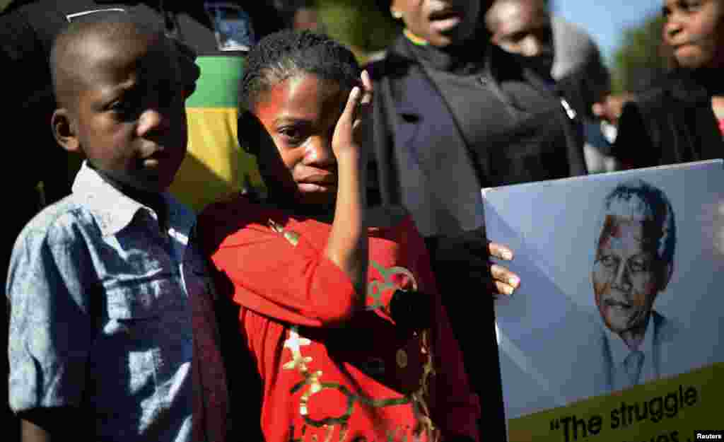 A girl weeps as she stands next to a portrait of Nelson Mandela held by ANC supporters outside the Mediclinic Heart Hospital in Pretoria, South Africa, June 28, 2013.