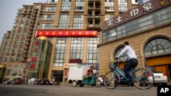 FILE - A delivery cart and cyclist ride past a building housing the Fengrui law firm in Beijing. Observers say China has shown little sign of easing its clampdown on rights defenders one year after the government arrested and interrogated nearly 320 human rights lawyers and activists.