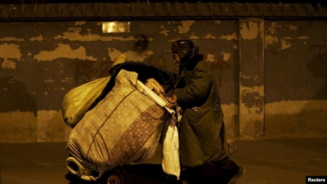 资料图片-中国北京寒冷的冬夜，一名流浪汉在北京南站附近的巷子里推着行李。（2016年1月23日）
