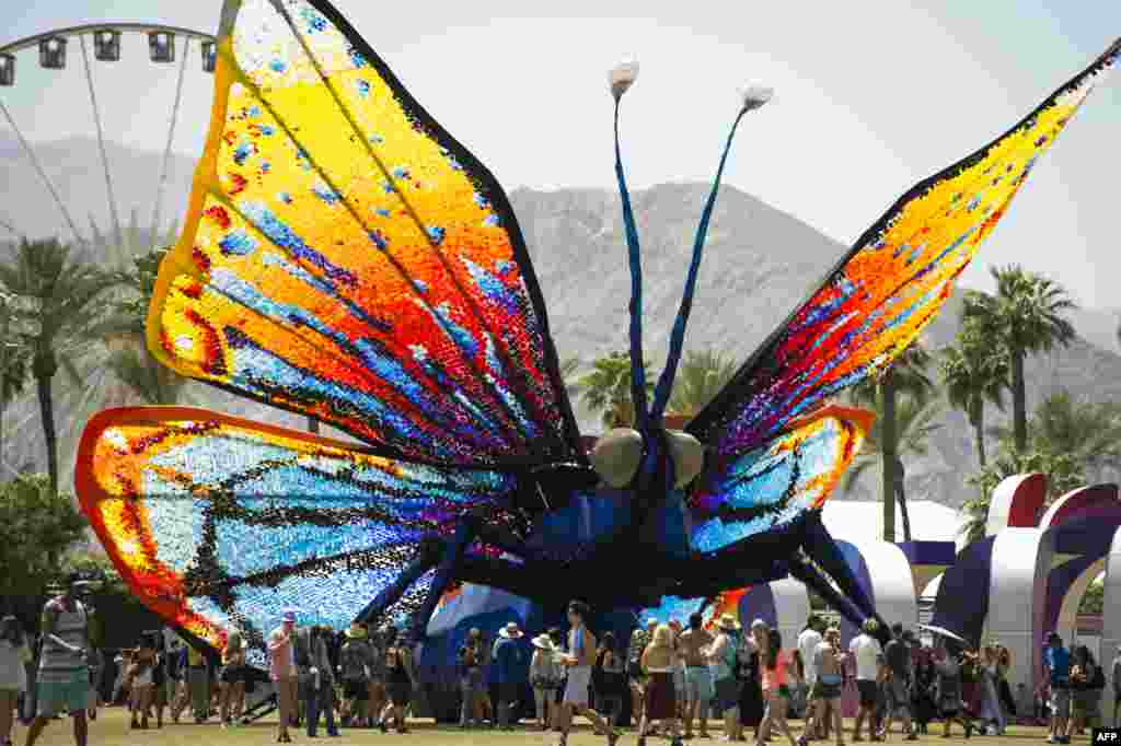 Penonton konser melewati patung kupu-kupu raksasa di hari ketiga Festival Musik Coachella di Indio, California, 12 April 2015.