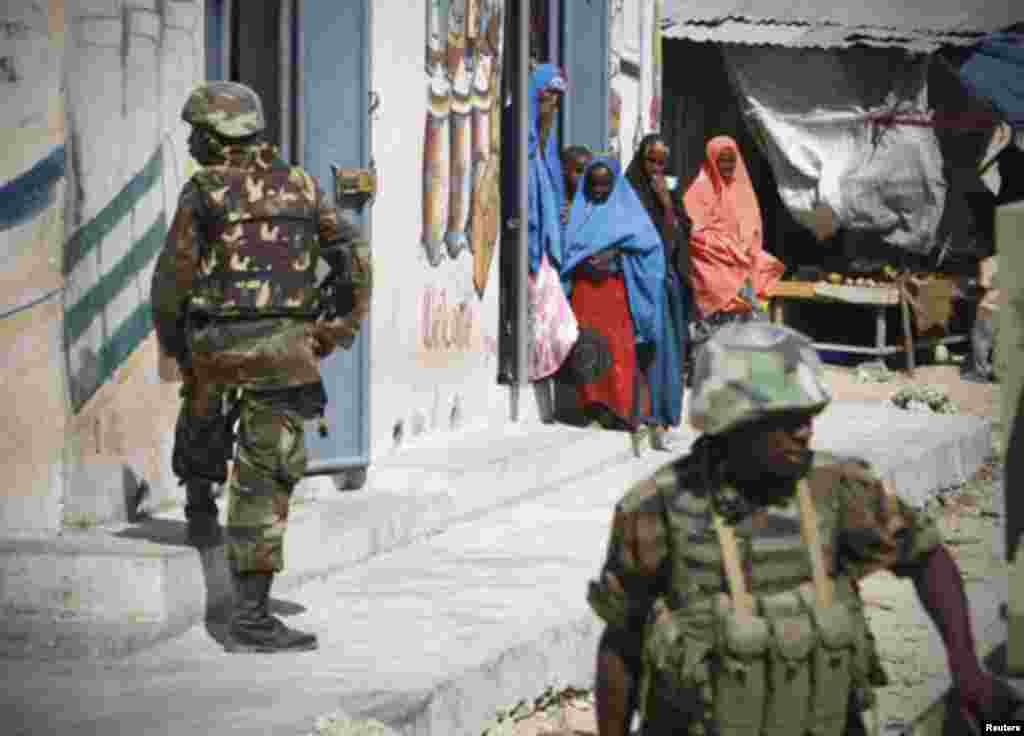 Somalia women look on as Ugandan soldier serving with the African Union Mission in Somalia (AMISOM) take up defensive positions in Torfiq market in the Yaaqshid District of northern Mogadishu December 5, 2011. Picture taken December 5, 2011. REUTERS/Afric