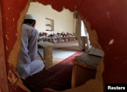 FILE - Boys are seen reading the Koran through a hole in a wall in a madrasa, or religious school, during the Muslim holy month of Ramadan in Kabul, July 26, 2012.