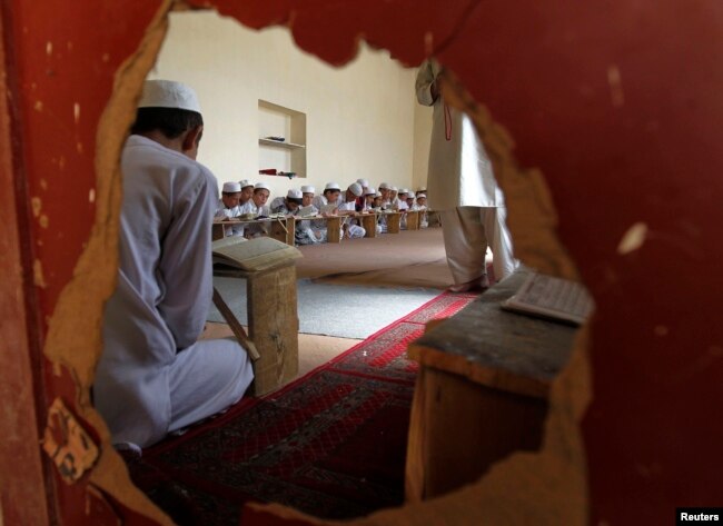 Anak laki-laki terlihat dari lubang di dinding di sebuah madrasah membaca Al-Quran di Kabul. (Foto: Reuters)
