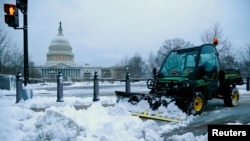 FILE - A worker clears snow from the sidewalks near the U.S. Capitol in Washington, March 17, 2014. Washington and the rest of the U.S. East Coast are expected to get a similar winter whacking this week.