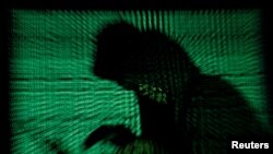 Un hacker encapuchonné tient un ordinateur portable alors qu'un cybercode est projeté sur lui. Cette photo d'illustration a été prise le 13 mai 2017. (Photo Reuters/Kacper Pempel)