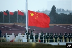 FILE - Chinese paramilitary policemen raise a flag in Tiananmen Square in Beijing, China, March 5, 2016. Improper use of the anthem in China is punishable by up to 15 days in prison.