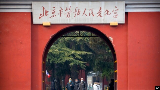 In this Jan. 27, 2020, photo, members of a group of foreign tourists wearing face masks to protect against the coronavirus walk through a public park near the Forbidden City in Beijing. The U.S. has issued a new travel advisory.