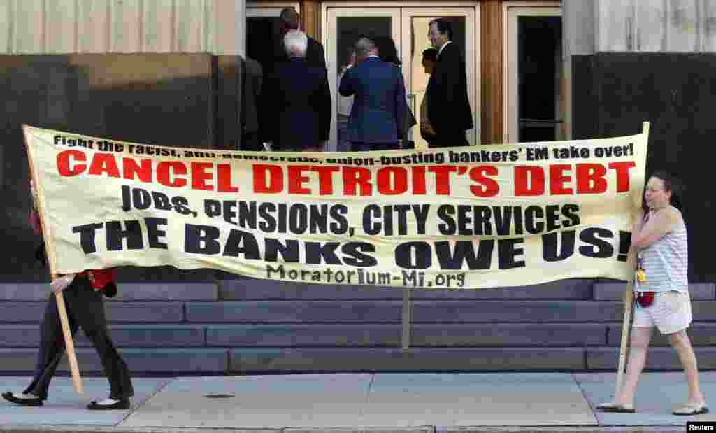 Protesters carry a banner calling for Detroit&#39;s debt to be canceled as people enter the federal courthouse for day one of Detroit&#39;s municipal bankruptcy hearings in Detroit, Michigan, USA. 