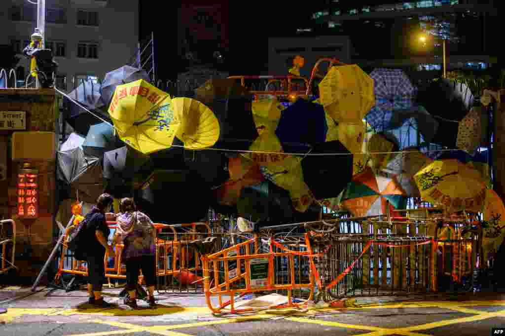 Two bystanders peer into barricades and umbrellas attached to an entry gate to the police headquarters in Hong Kong.