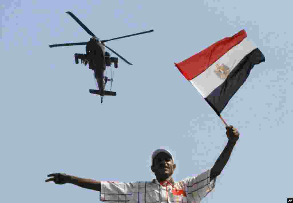 A military helicopter flies over an opponent if Egyptian Islamist President Mohammed Morsi as he waves a national flag, in Tahrir Square in Cairo, July 2, 2013.