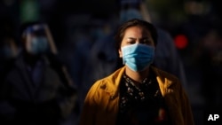 FILE - A woman wearing a face mask waits with dozens of others to get a coronavirus test at the National Stadium in Phnom Penh, Cambodia, Tuesday, Dec. 8, 2020.